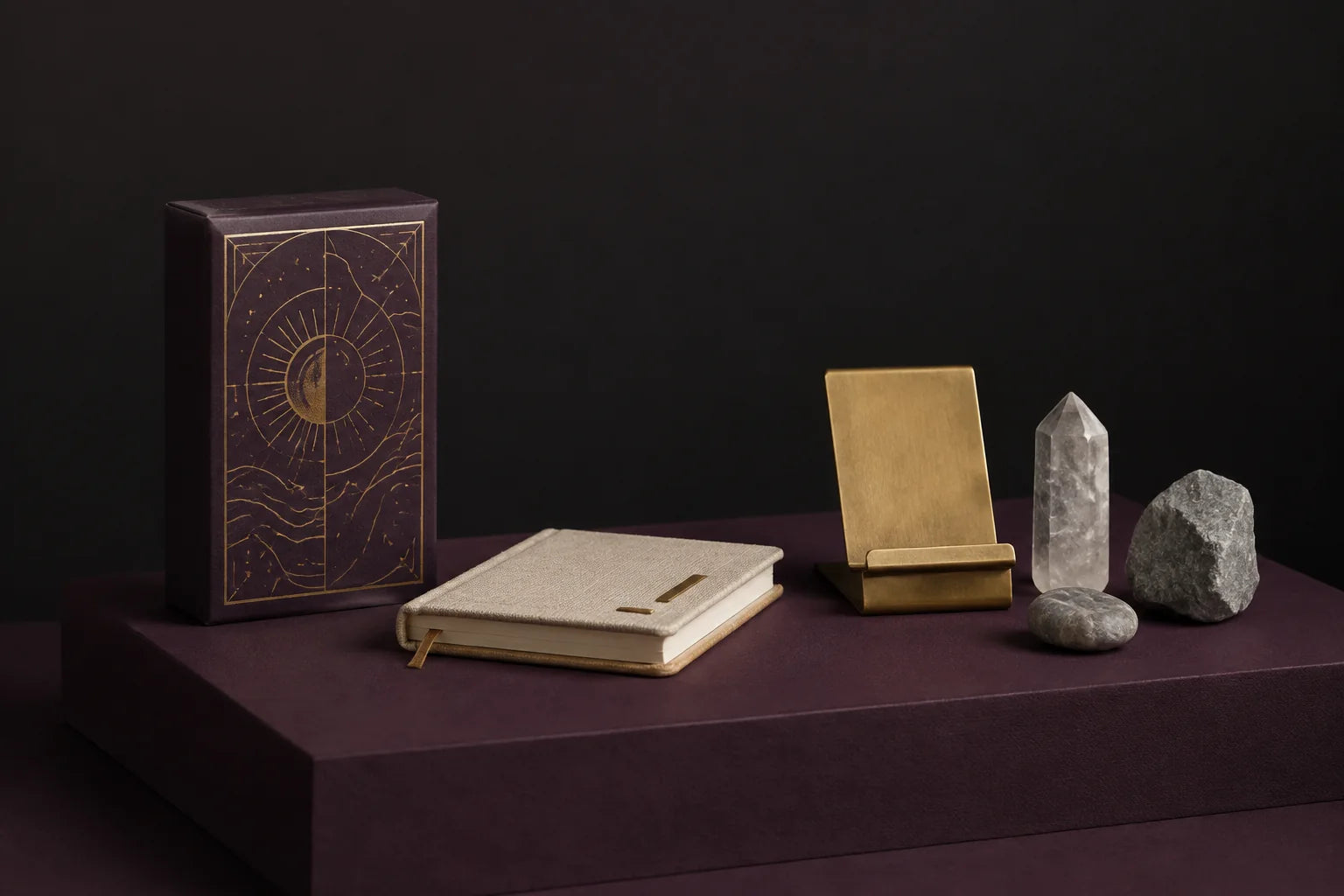 A tarot deck, journal, brass stand, and natural stones on a plum pedestal